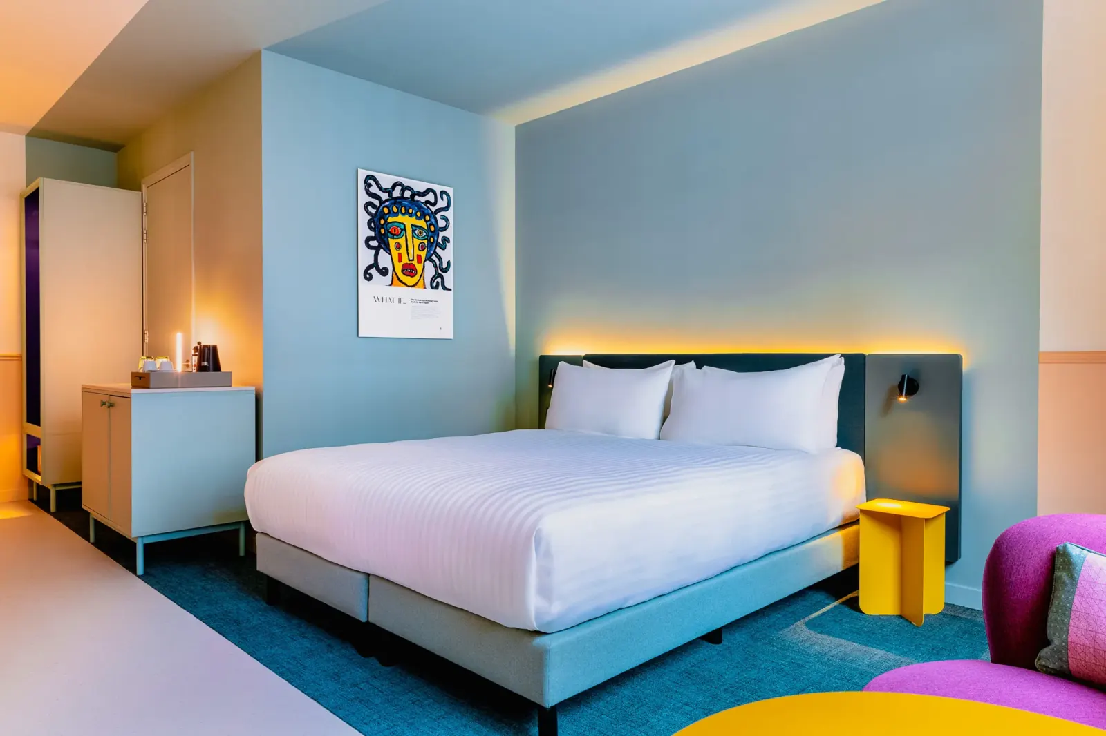 Hotelkamer van The Rebyl met kleurvlakken in geel, blauw en paars rond het bed