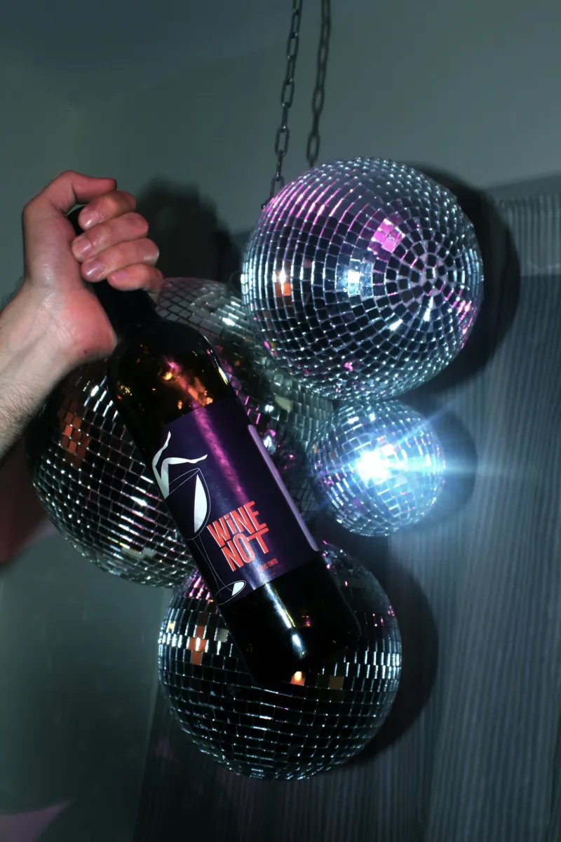 Fles Wine Not vastgehouden tussen twee spiegelende discoballen