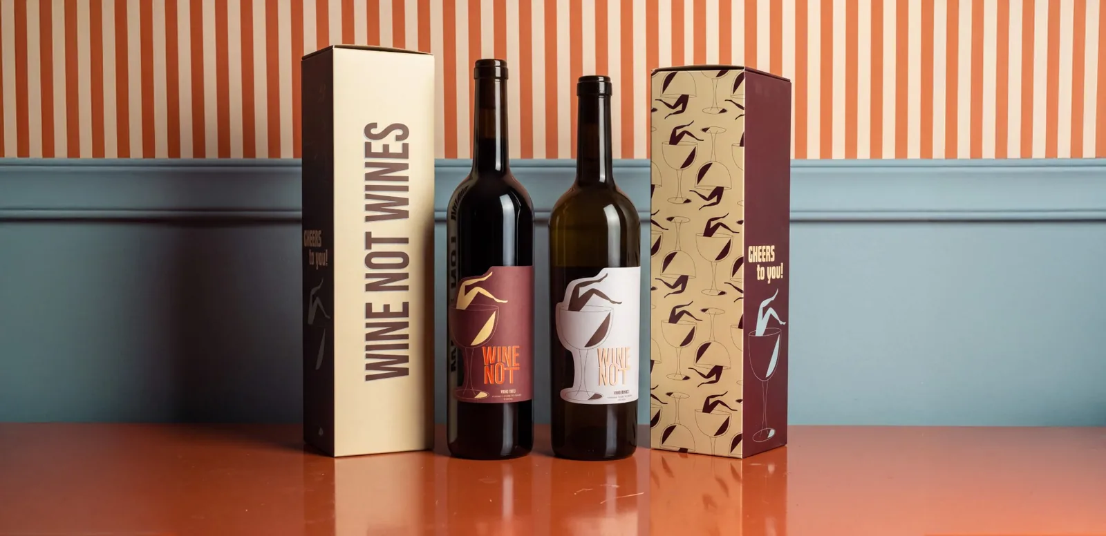 De twee flessen Wine Not tussen de twee geschenkdozen, op een oranje kast voor een gestreepte wand